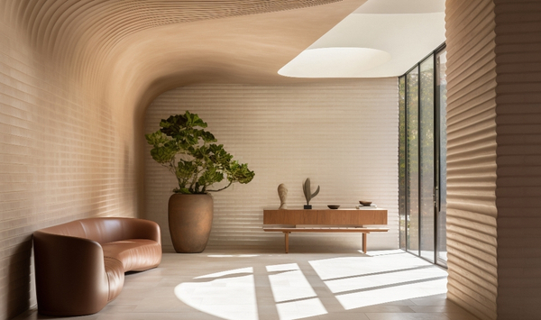 Modern ADU interior with curved textured walls, warm neutral finishes, sculptural furniture, natural light, and floor-to-ceiling windows overlooking the outdoors.