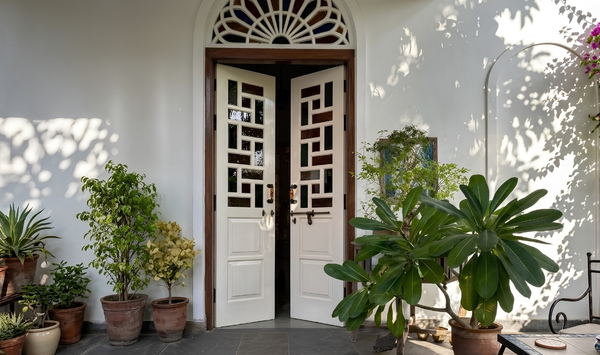 Charming ADU entrance with decorative white double doors, lush potted plants, and a shaded courtyard-style entry.