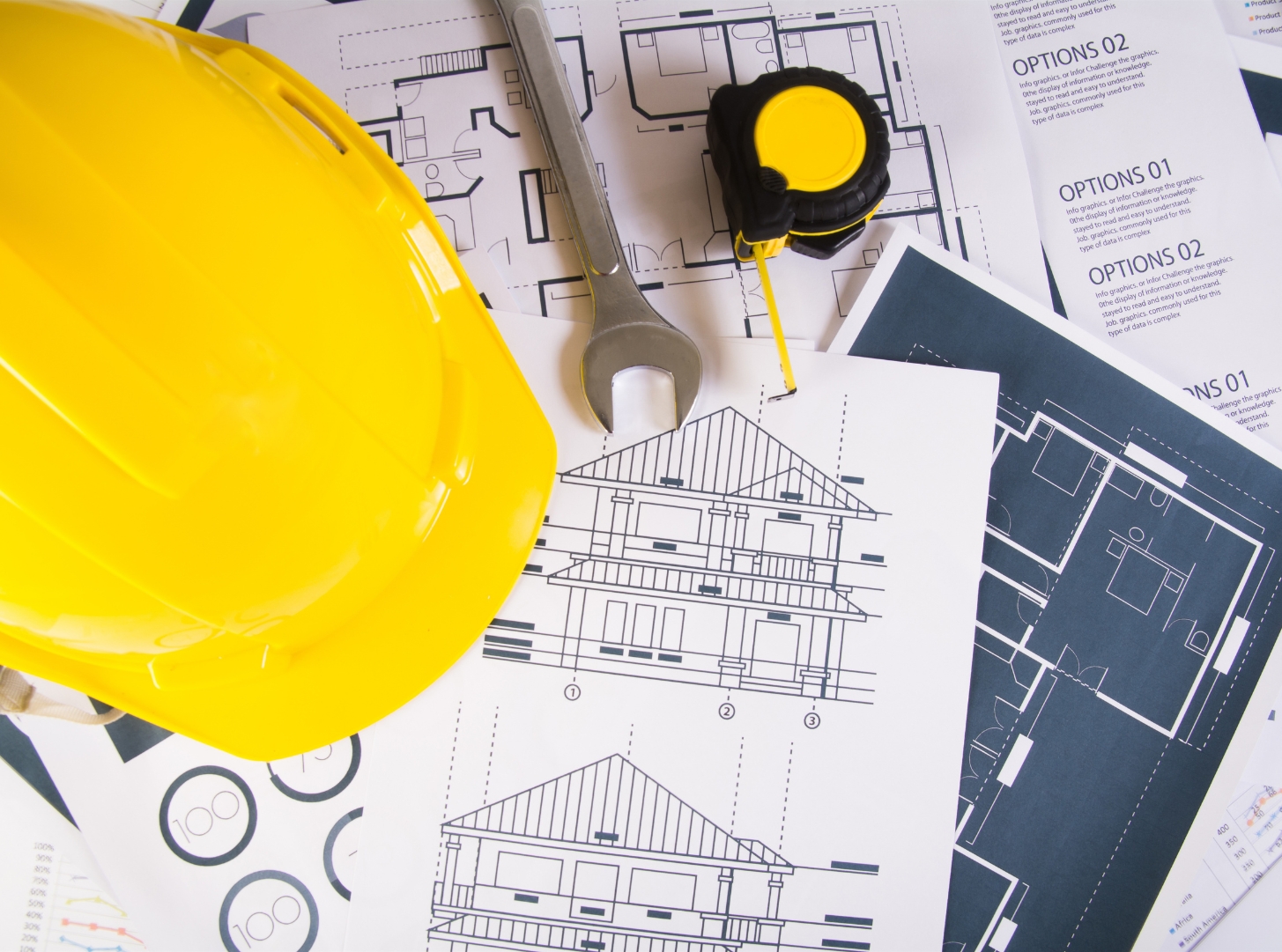 ADU architectural plans with a yellow hard hat, tape measure, and building drawings representing ADU design, planning, and construction preparation.