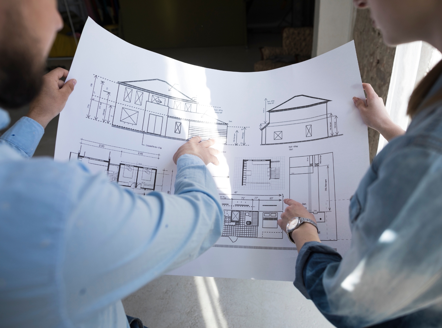 Two people reviewing architectural plans for an ADU, including floor plans and exterior elevations, during the ADU design and planning process.