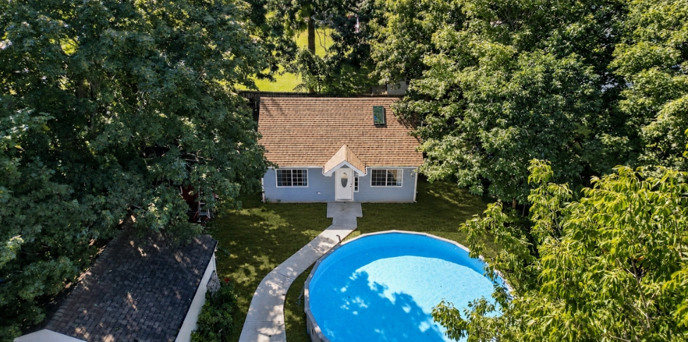 Blue backyard ADU under construction with ladders, new siding, front windows, entry door, and a small gabled roof.