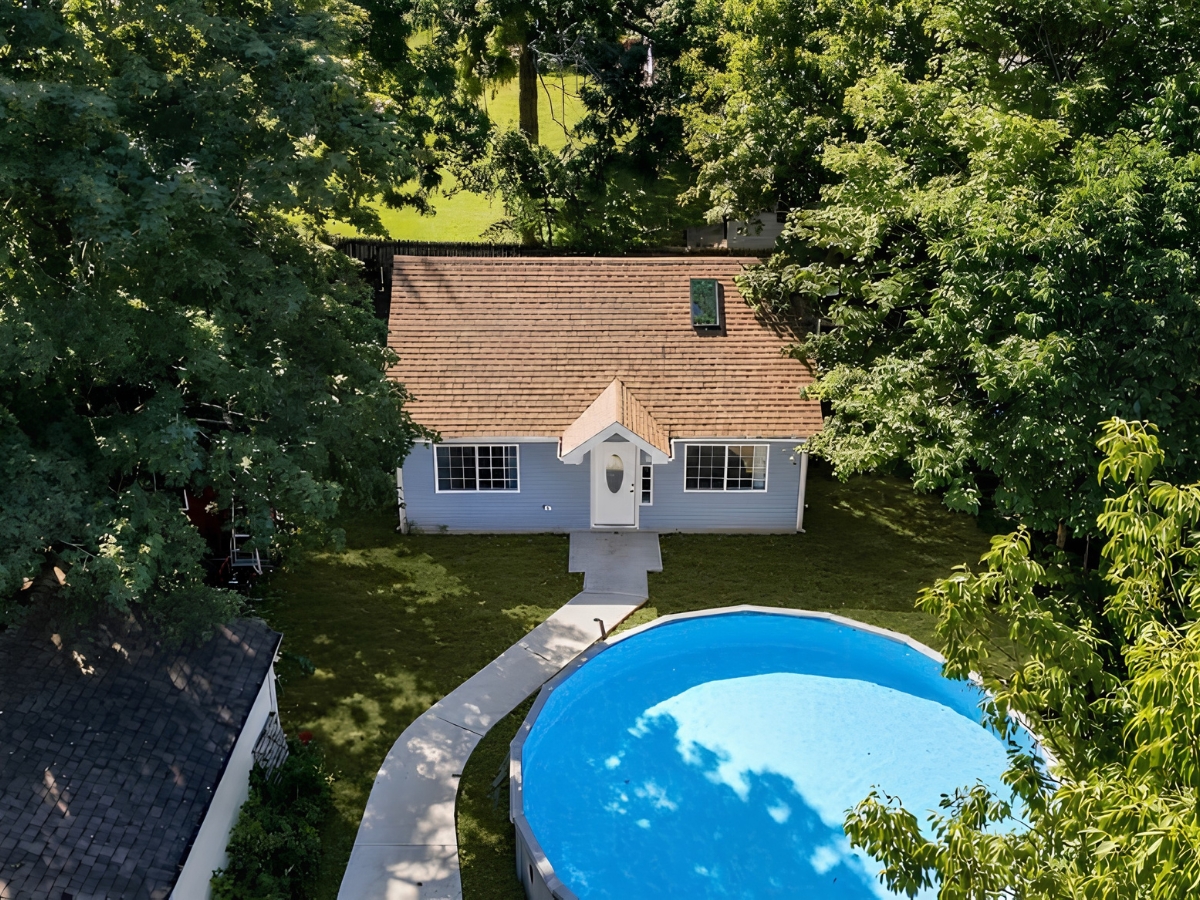 Detached backyard ADU beside an above-ground swimming pool, surrounded by mature trees and a landscaped lawn.