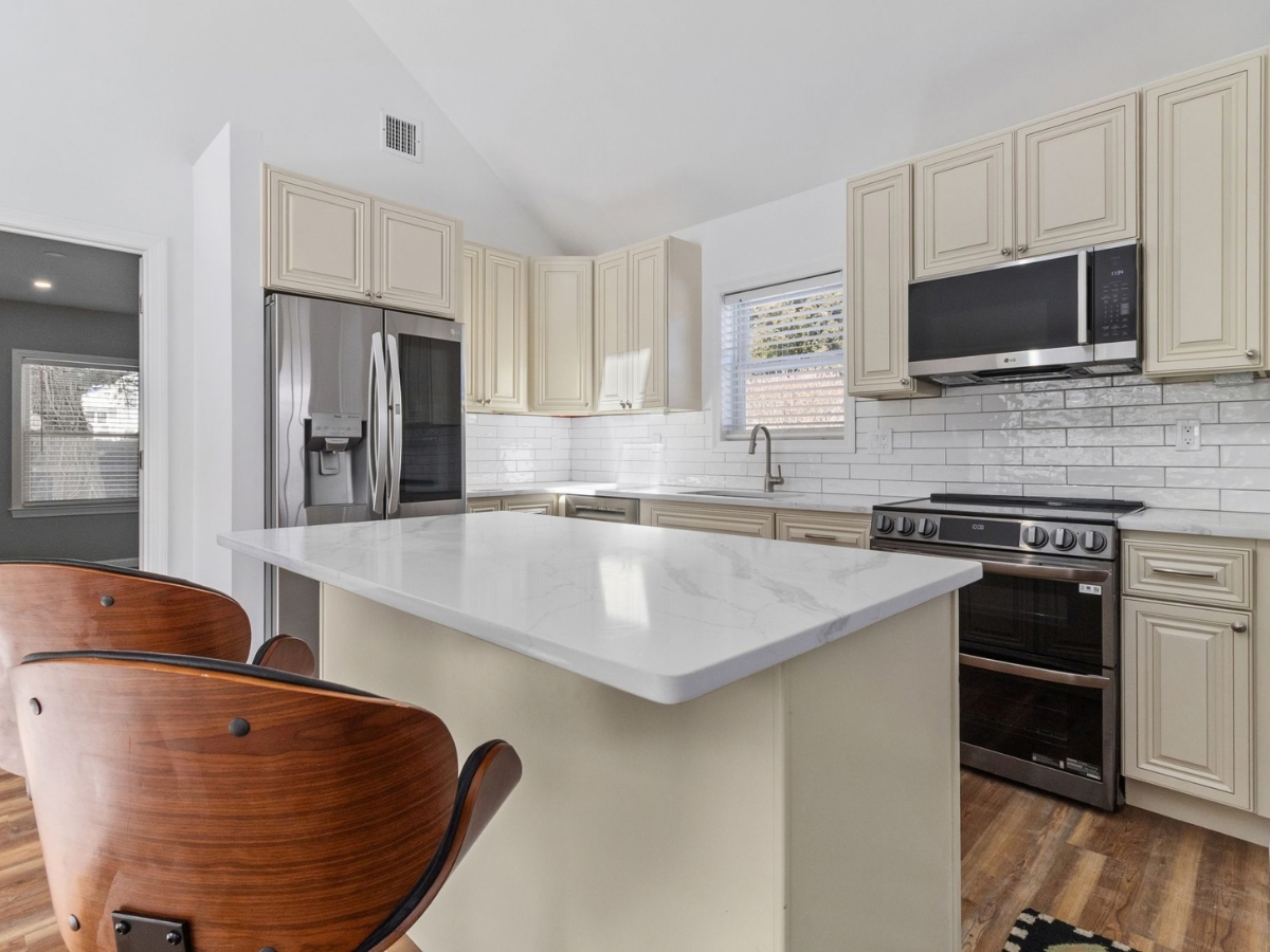 Modern ADU kitchen with white cabinetry, quartz island, stainless steel appliances, subway tile backsplash, and wood flooring.
