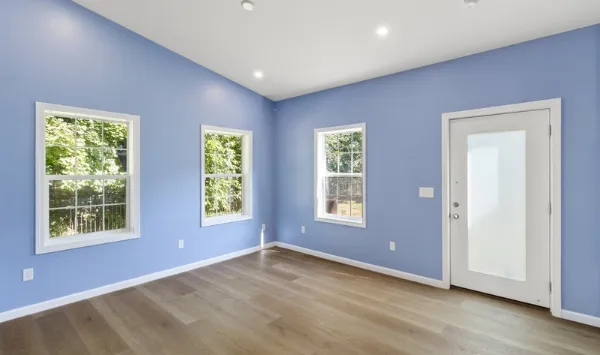 Blue-walled room with windows, wood flooring, and white doors, suitable for a custom ADU home office. 