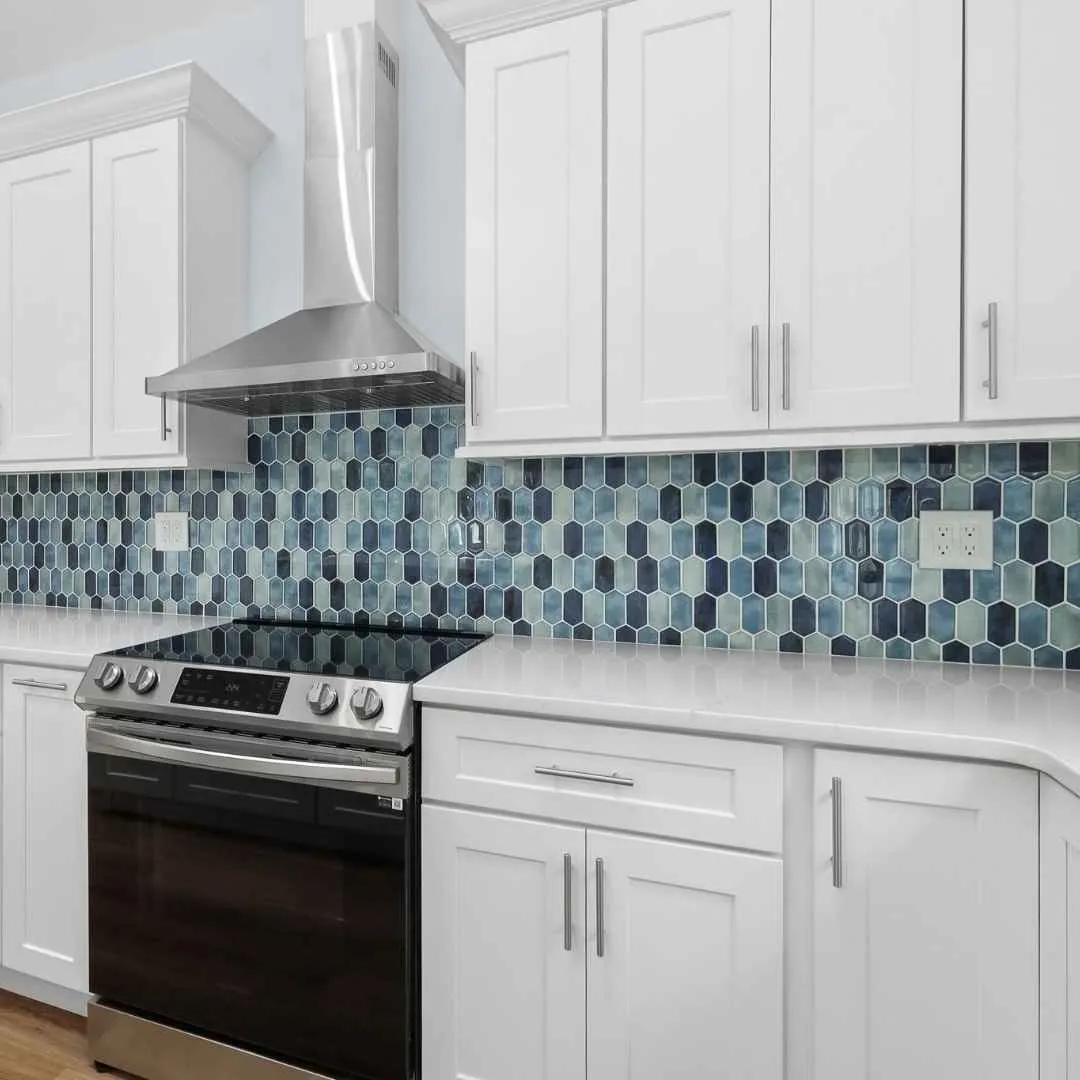 Modern ADU kitchen with white shaker cabinets, stainless steel range and hood, and blue hexagon tile backsplash.