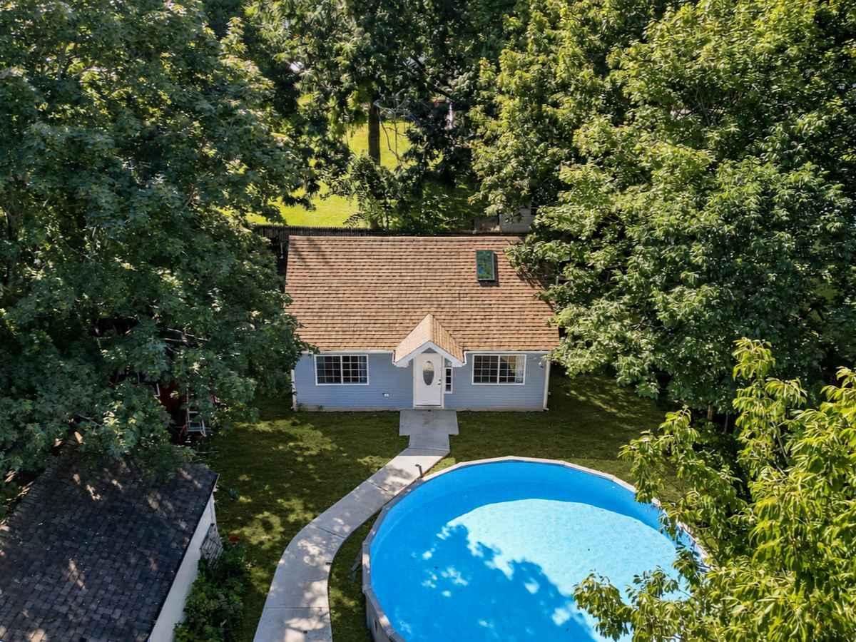 Detached backyard ADU beside an above-ground swimming pool, surrounded by mature trees and a landscaped lawn.