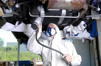 Mitarbeiter im weißen Schutz-Overall und Maske, stehend unter einem Auto