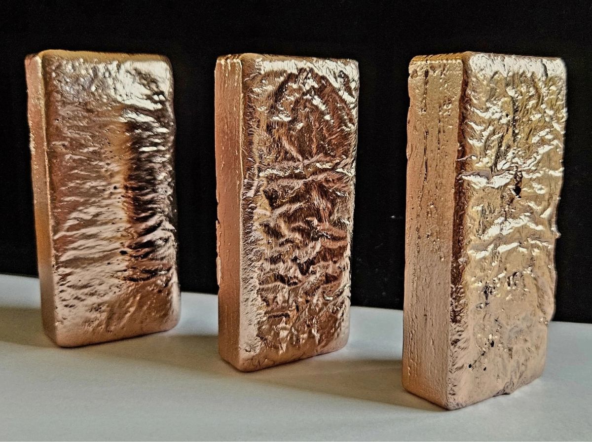 Satin finish hand-poured copper bar with natural cooling ripples on raw graphite