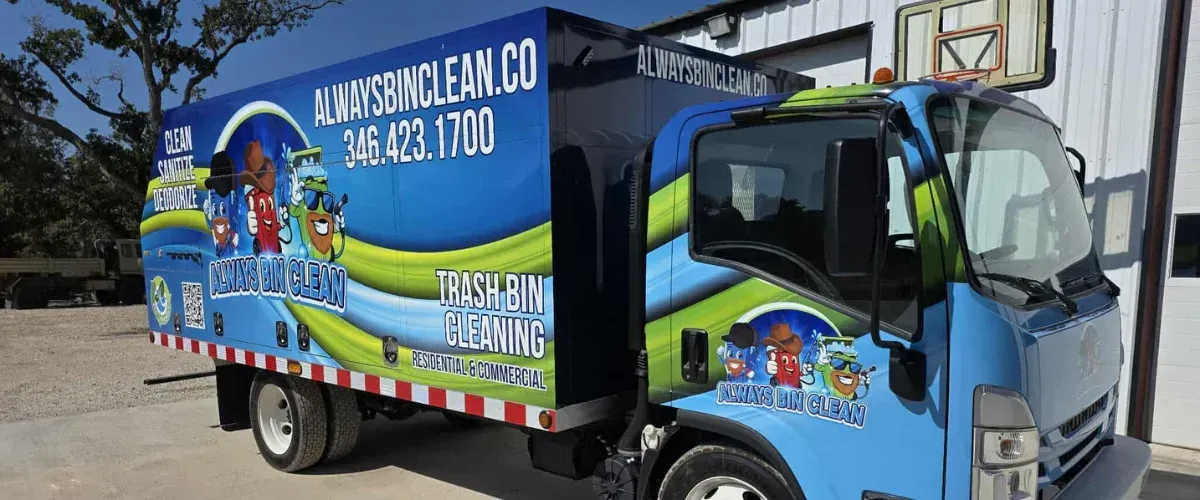 A truck from "Always Bin Clean" parked in a suburban driveway with a man and two trash cans beside it.