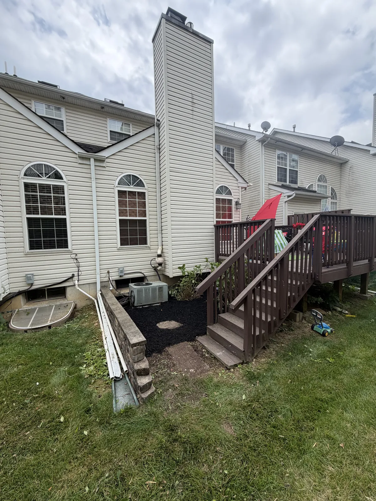Downspout extension running beside a retaining wall to a splash block near backyard deck stairs.