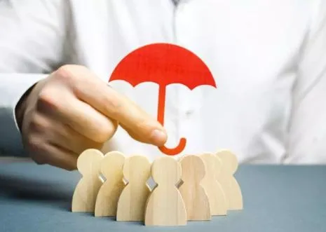 A hand holding a red umbrella over small wooden figures