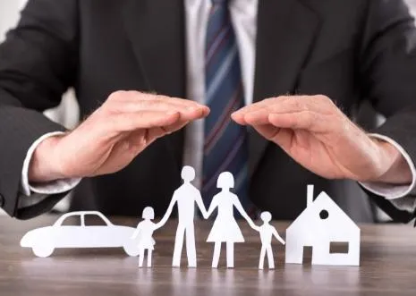 Two hands sheltering paper cutouts of a family and a house