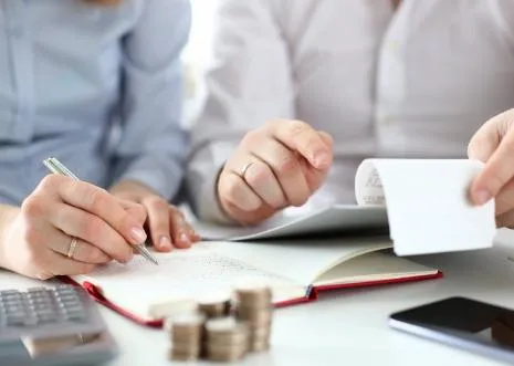 Two people reviewing a notebook and receipts