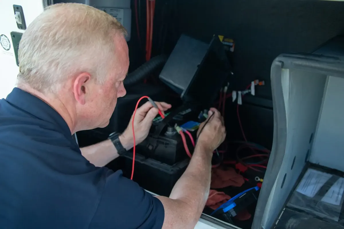 Technician performing electrical diagnostics and repairs on RV power systems, focusing on battery connections and wiring.