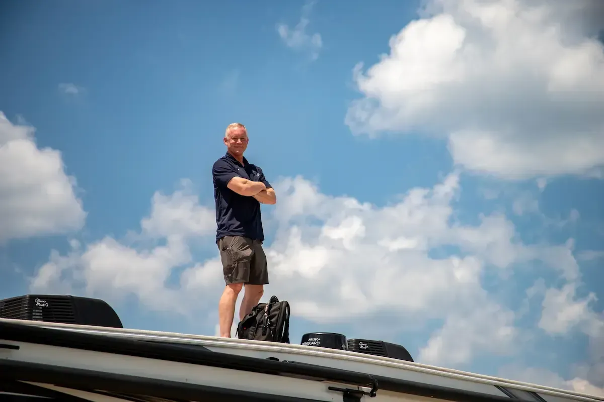 Man standing confidently on the roof of an RV under a blue sky with clouds, representing Sentry RV's commitment to mobile inspections and repairs.