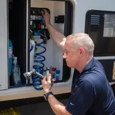 Man inspecting RV exterior with smartphone, highlighting mobile RV repair services.