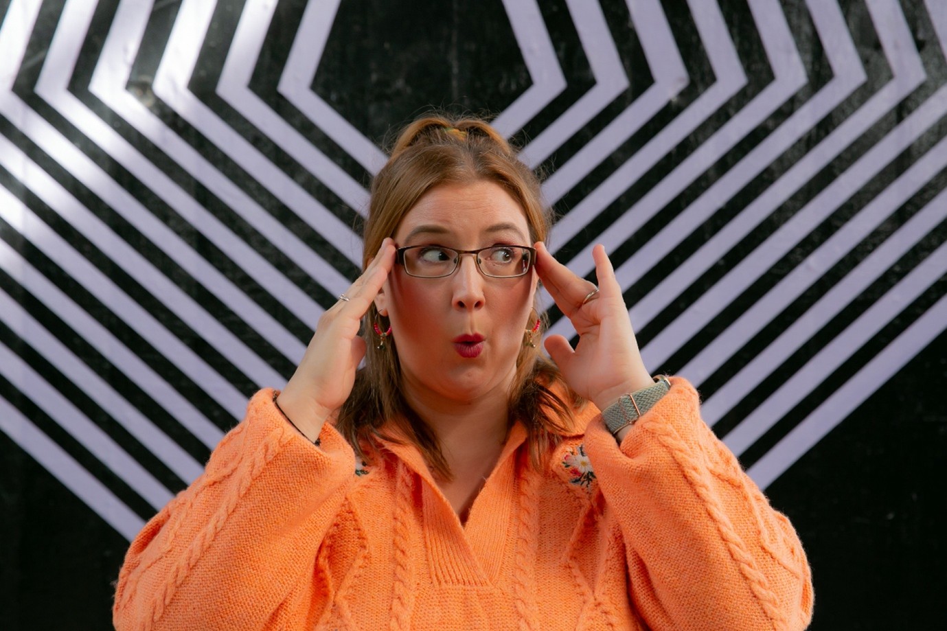 Rachel holding her hands to her temples in front of a bold geometric background, representing the complexity of executive functions such as attention, planning, emotional regulation and information processing in the neurodivergent brain.
