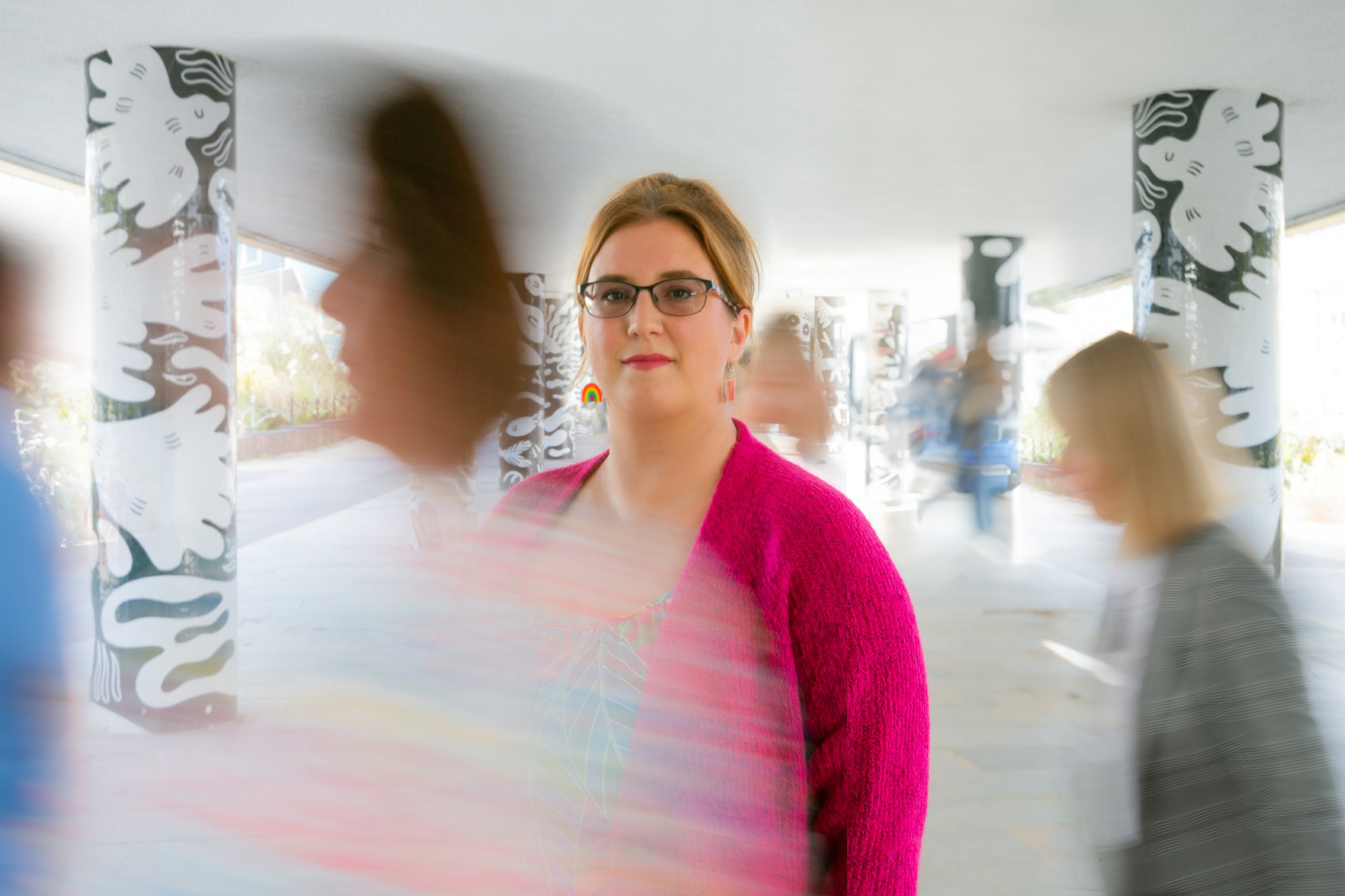 Rachel Clayton stands calmly in sharp focus while blurred people move quickly around her, illustrating the feeling of being overwhelmed as life continues at pace. The image accompanies text explaining that neurodivergent burnout often develops gradually over months or even years.