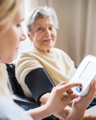 Eine Frau misst bei einer älteren Frau den Blutdruck mit einem digitalen Blutdruckmessgerät.