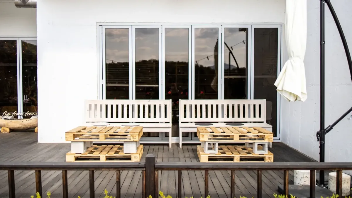 Minimalist patio setup with white benches and pallet-style wooden tables arranged on a gray deck.