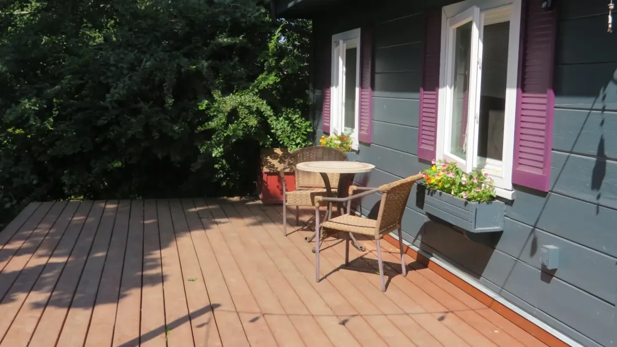 Cozy outdoor deck with a small bistro table, wicker chairs, and windows accented by purple shutters and flower boxes.