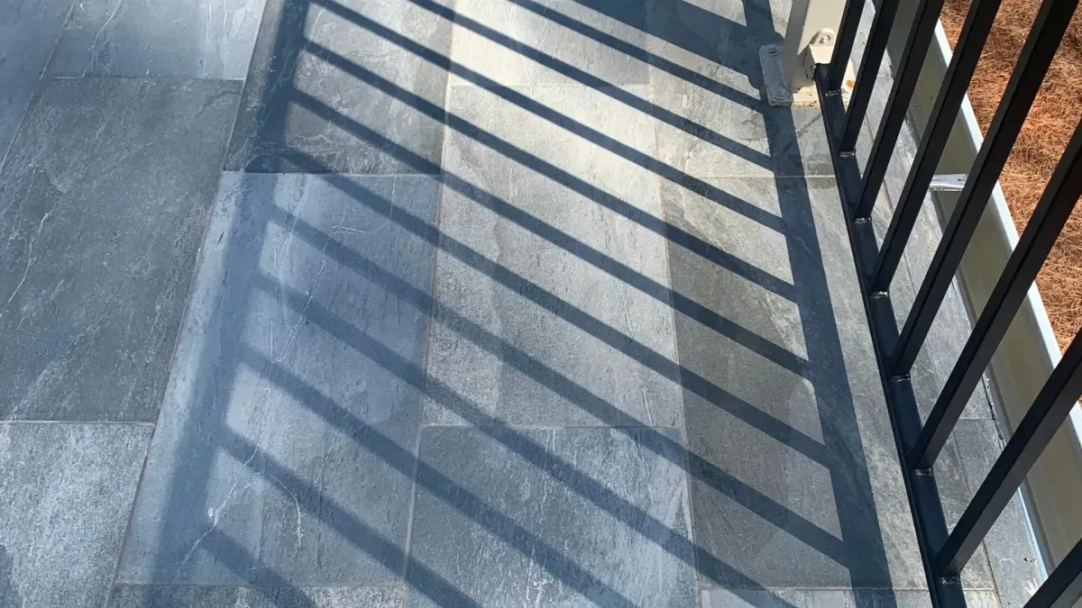 Gray tiled floor with shadows of black metal railing forming diagonal lines in sunlight.