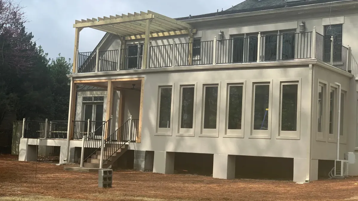 Large two-story home with an elevated deck, black railings, and a newly built pergola frame above the upper outdoor space.
