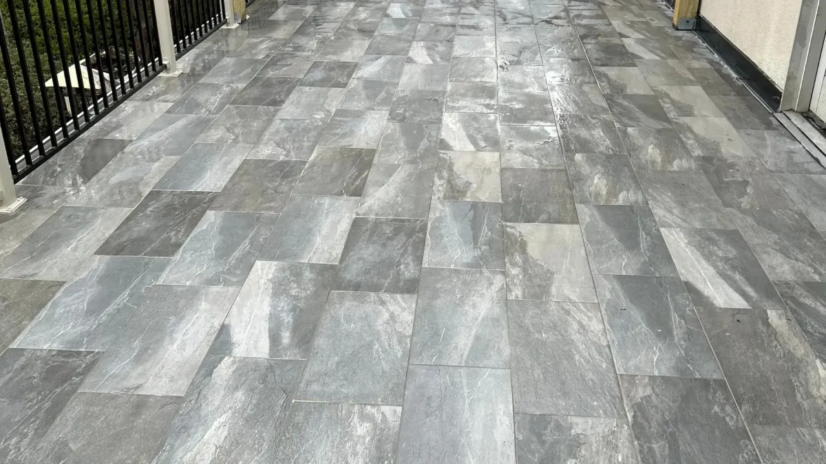 Outdoor patio with gray stone-look tile flooring, black railings, white posts, and pergola under blooming trees.