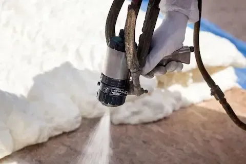 Professional applying expanding spray foam insulation to seal and insulate a wooden floor in Hoboken, NJ.