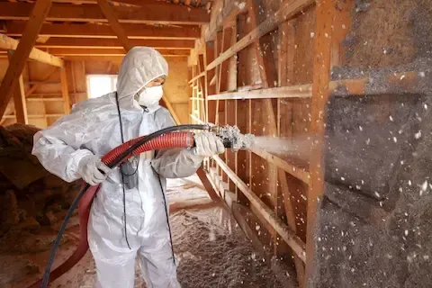 Insulation contractor applying blown-in cellulose insulation to exposed wall cavities during a home renovation.