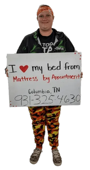 A picture of a happy woman that bought a mattress holding an "I love my new mattress" sign