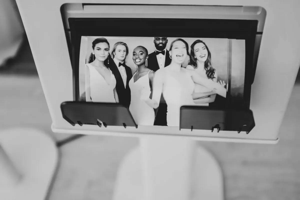 A black-and-white photo displays a group of six people dressed formally, posing and smiling at a Photo Booth Rental DC.