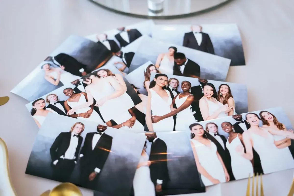 A collection of printed photographs featuring people in formal attire, including suits and dresses, spread out on a reflective surface near some silverware, reminiscent of a Photo Booth Rental at an elegant event.