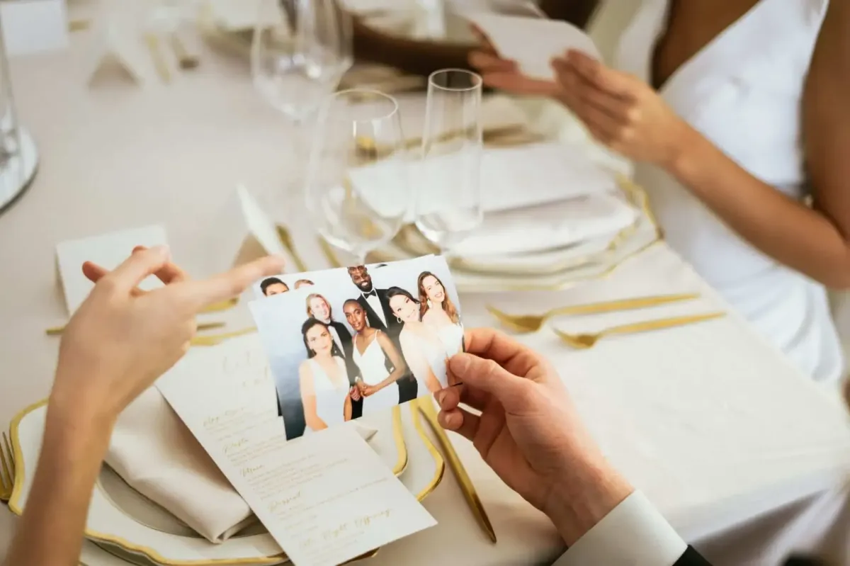 A person holds a photo with a group of people, seated at a table with elegantly set place settings, menus, and wine glasses, likely taken during an event featuring a Photo Booth Rental DC.