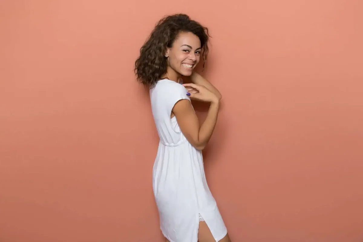 A woman in a white dress smiles while standing against a peach-colored photo booth backdrop.