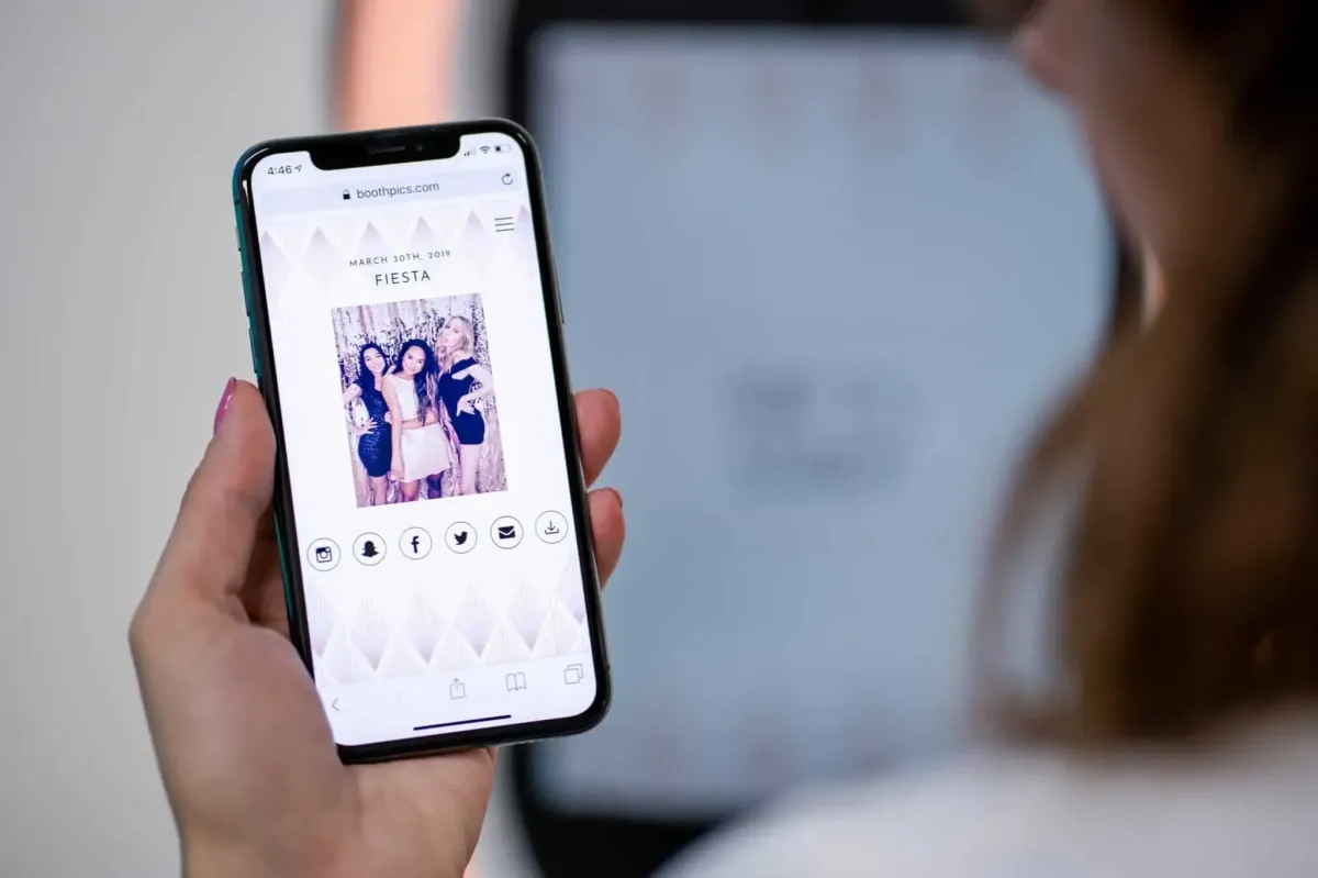 A person holding a smartphone displays an online gallery viewer featuring an invitation with a group photo and the word "Fiesta," dated March 24th, 2019.