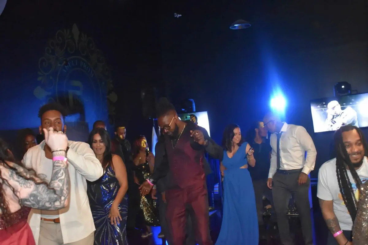 A group of people dance in a dimly lit room with blue lighting, celebrating to tunes spun by a private event DJ. Some wear formal attire, adding an elegant touch to the lively atmosphere.