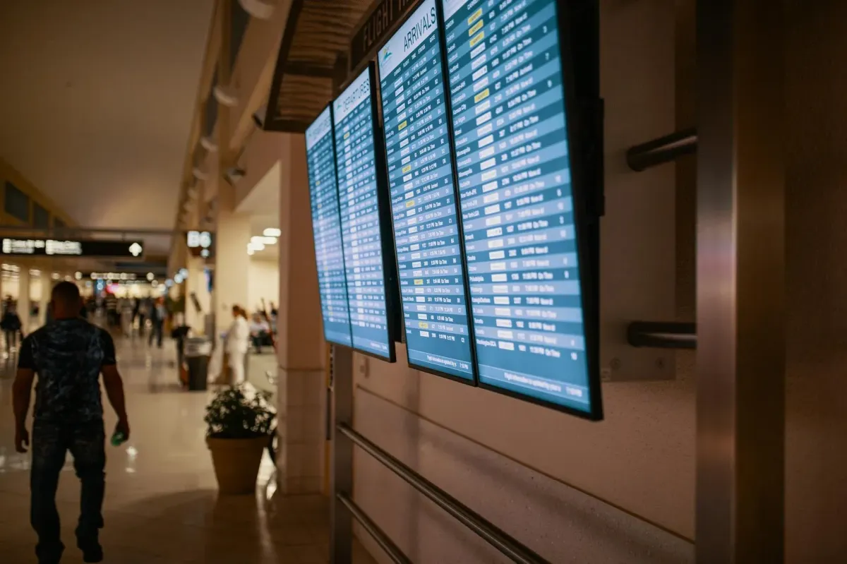 A middle-aged African American man in a home office, speaking on the phone with a notepad and laptop open, focused and smiling, with travel posters on the wall, representing a smooth booking process.