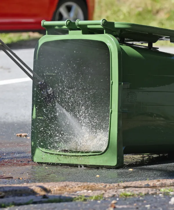 Person pressure washing the inside of a green trash bin for deep cleaning.