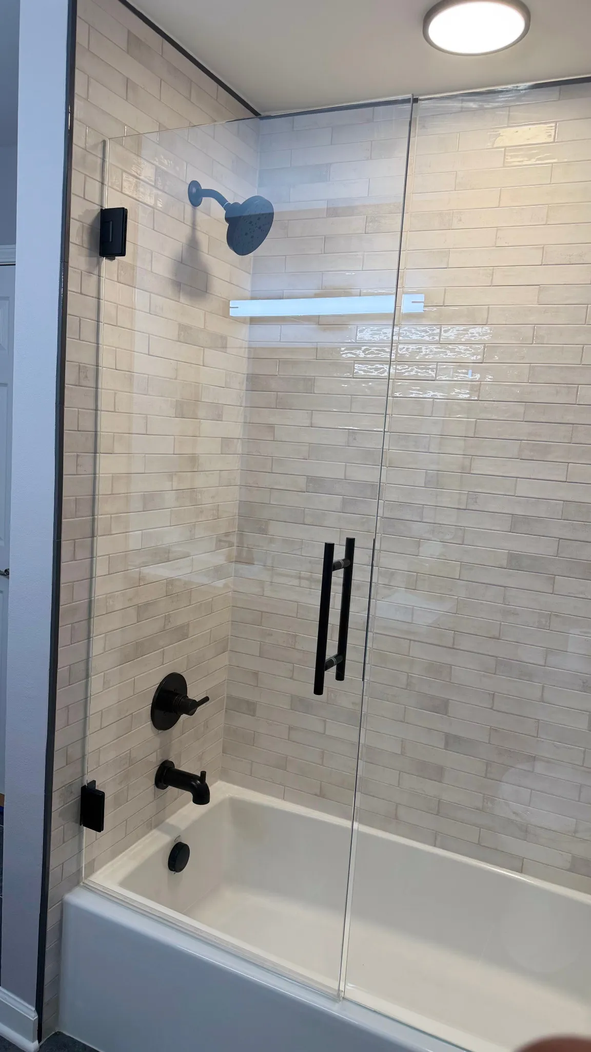 Tub and shower combination with white subway tile, frameless glass doors and matte-black fixtures
