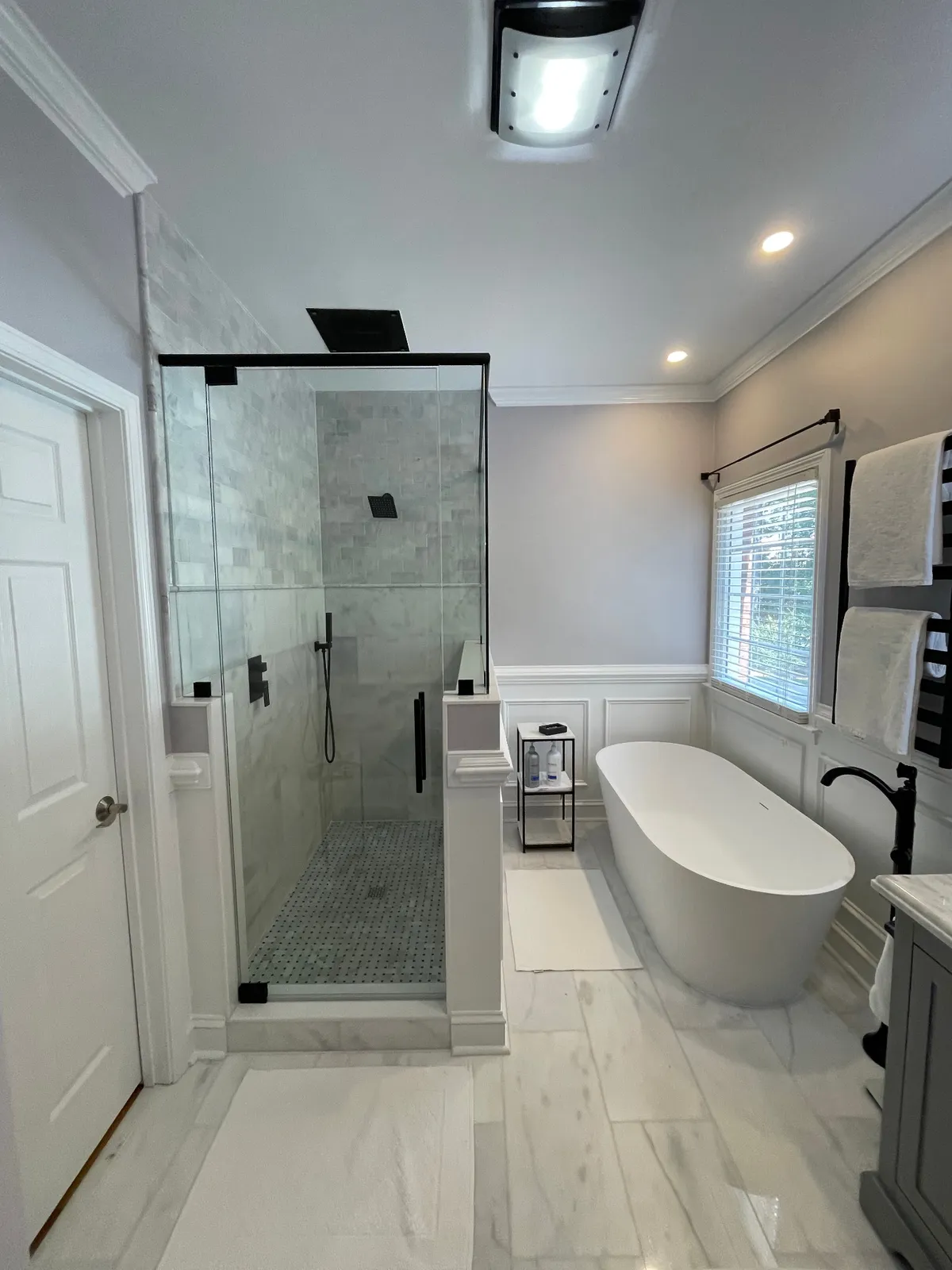 Freestanding bathtub and frameless shower with black hardware in a bright bathroom