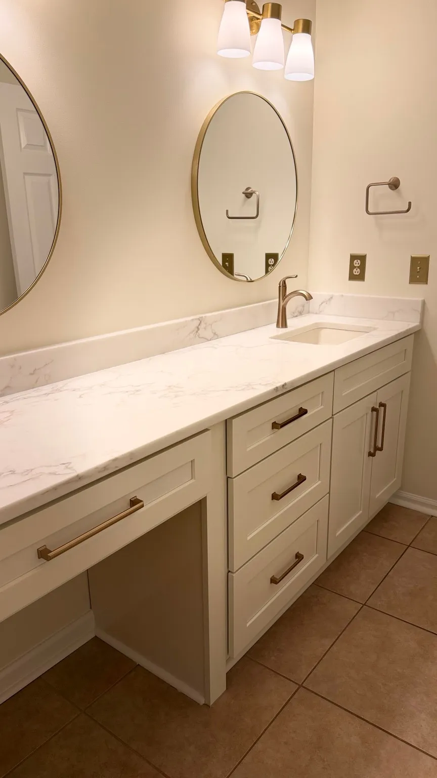 White bathroom vanity with a veined countertop, brass fixtures and oval mirrors by JR Remodeling
