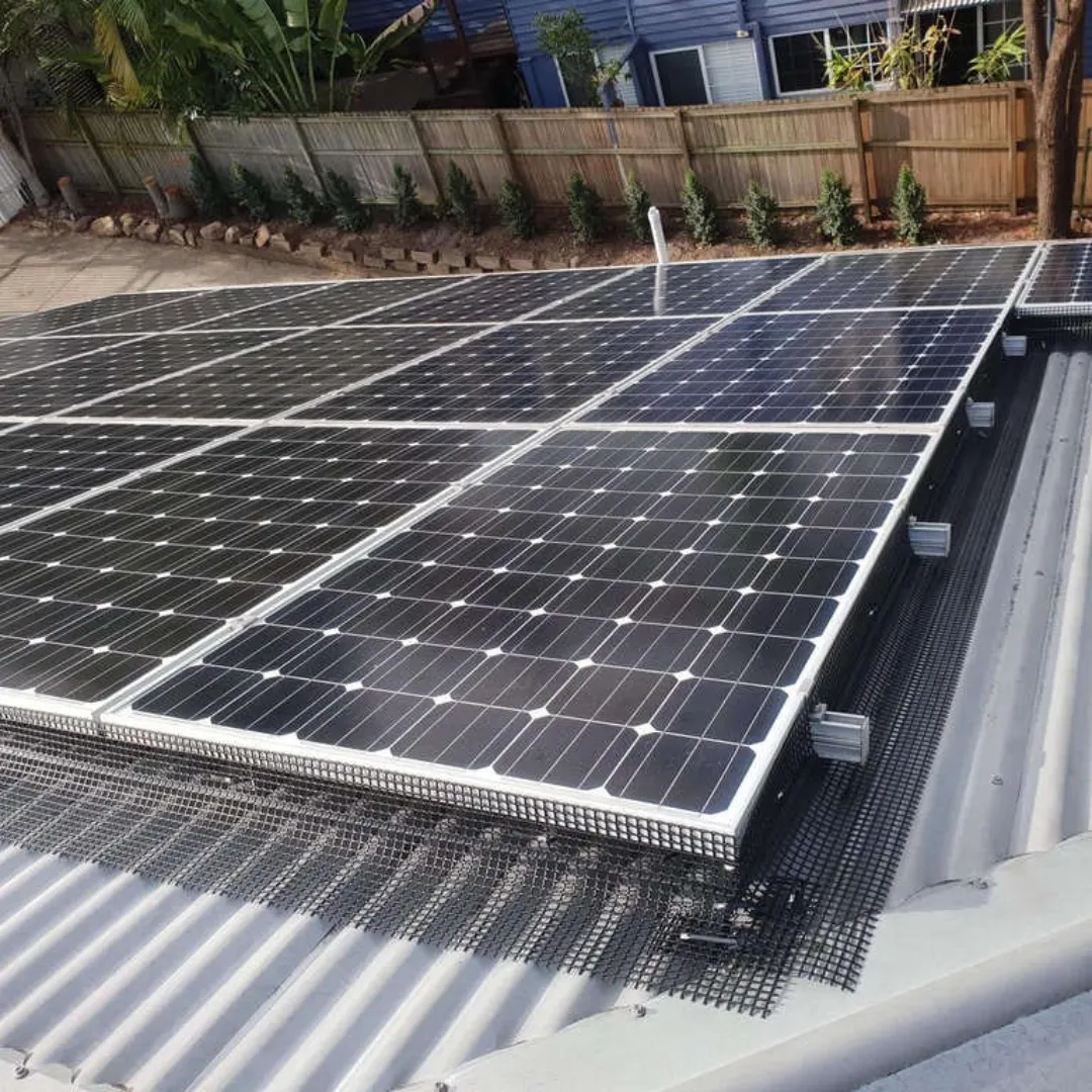 Aerial view of solar panels that have been protected with mesh bird proofing. The black mesh is installed around the perimeter of the solar panels to prevent birds from nesting underneath while still allowing proper airflow. The clean, well-maintained solar array is installed on a metal roof with a residential backyard and fence visible in the background.