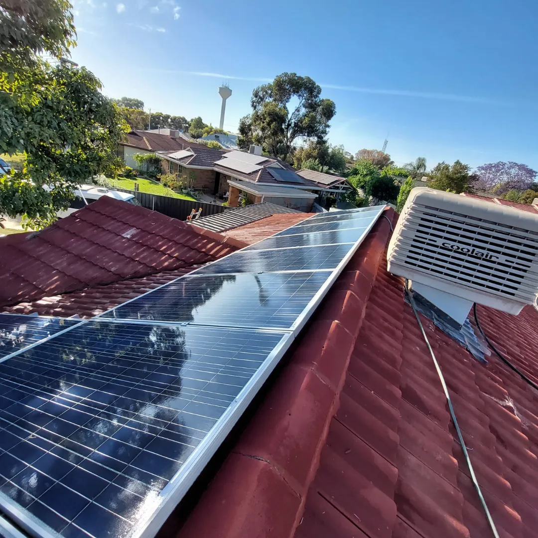 Rooftop solar panel installation on a red-tiled roof beside a Coolair evaporative cooler in a Mildura residential area.