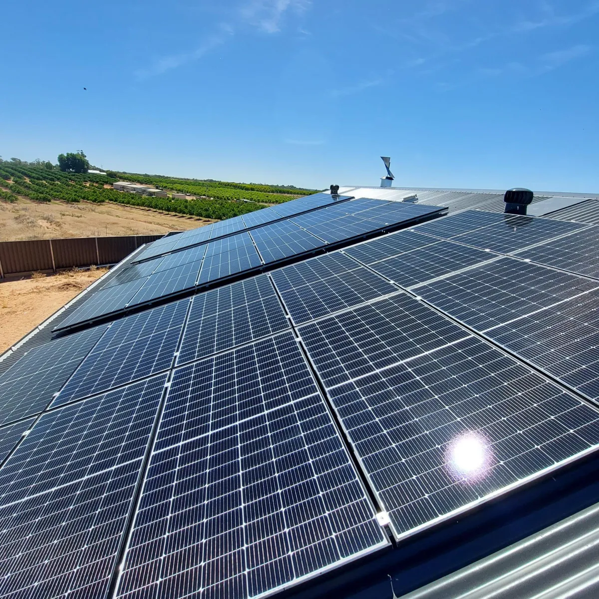 Rows of modern solar panels glistening in the sun on a metal roof overlooking farmland in Mildura.