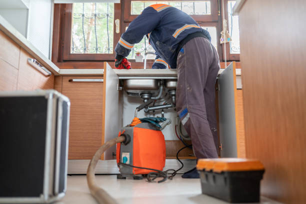 Plumber using professional equipment to unclog a kitchen sink drain under the cabinet.