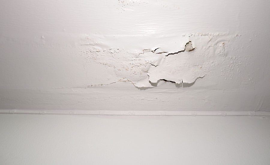 Water-damaged ceiling with peeling paint and bubbling surface from a leak.