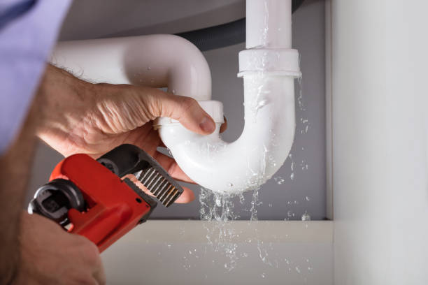 Plumber fixing a leaking P-trap pipe under the sink with a wrench as water sprays out.