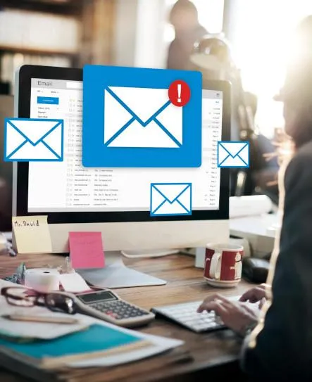 A computer screen with emoji style emails popping out of it. there is a big one in the middle with a red exclamation mark that is marking an email as important. there is a man looking at the screen.