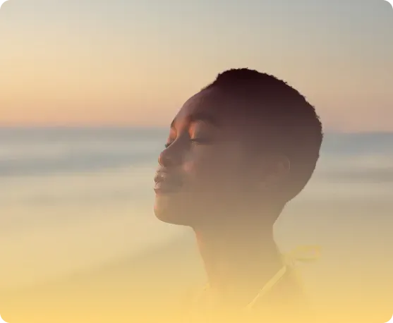 Person meditating on a beach at sunset with eyes closed—mindfulness, calm breathing, relaxation, and mental wellness.